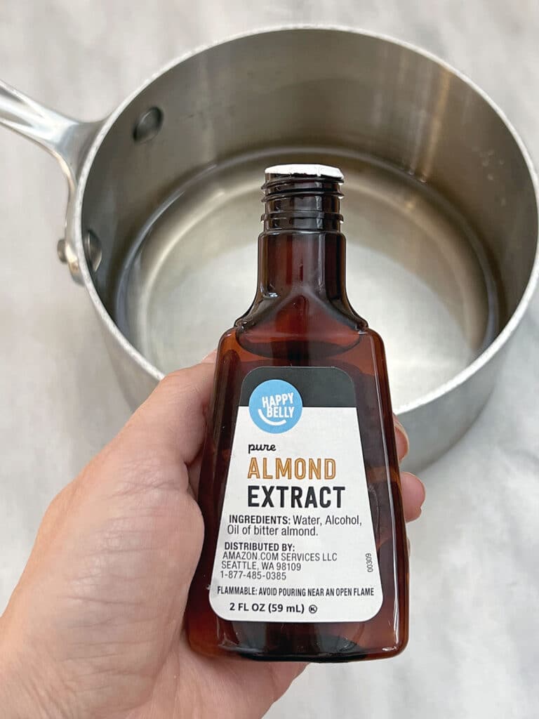 Almond extract bottle being held over simple syrup in saucepan.