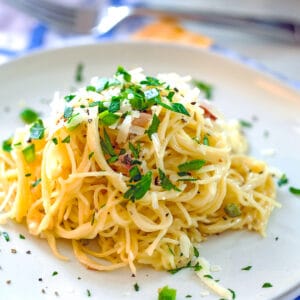 Close-up view of angel hair alfredo pasta on plate with pancetta, jalapeño, and parsley