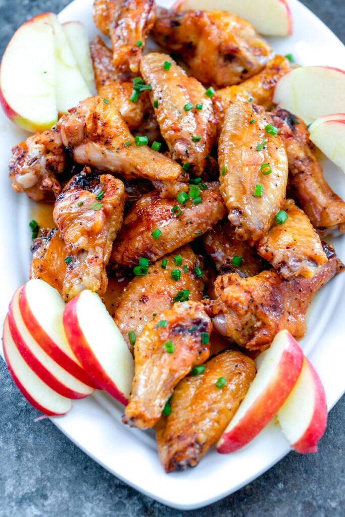 Bird's eye view of platter of apple cider chicken wings with sliced apples and chives
