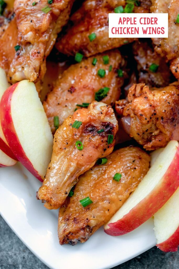 overhead close-up view of apple cider chicken wings on a platter with sliced apples and chives with recipe title at top