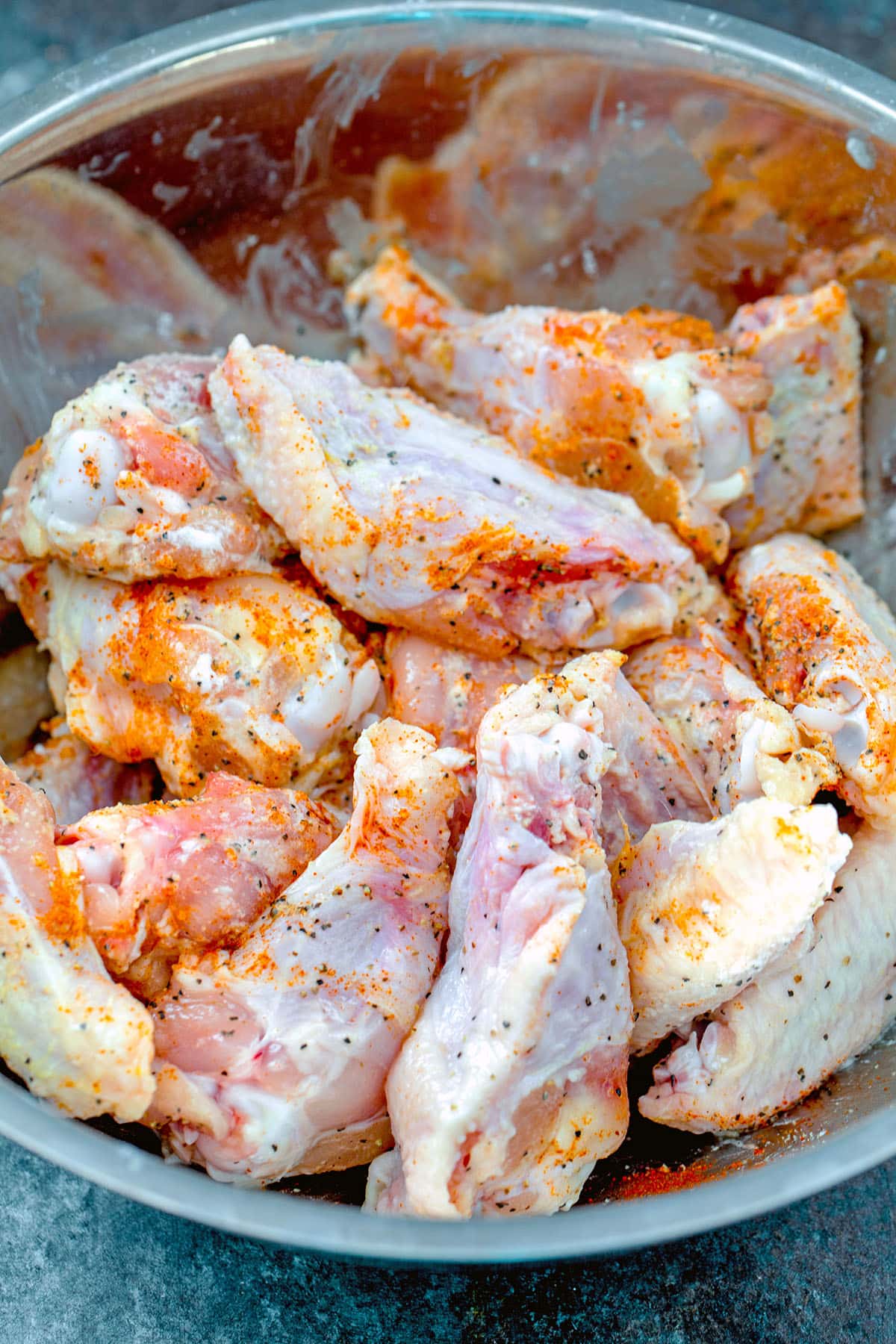 Chicken wings tossed with spices in bowl.