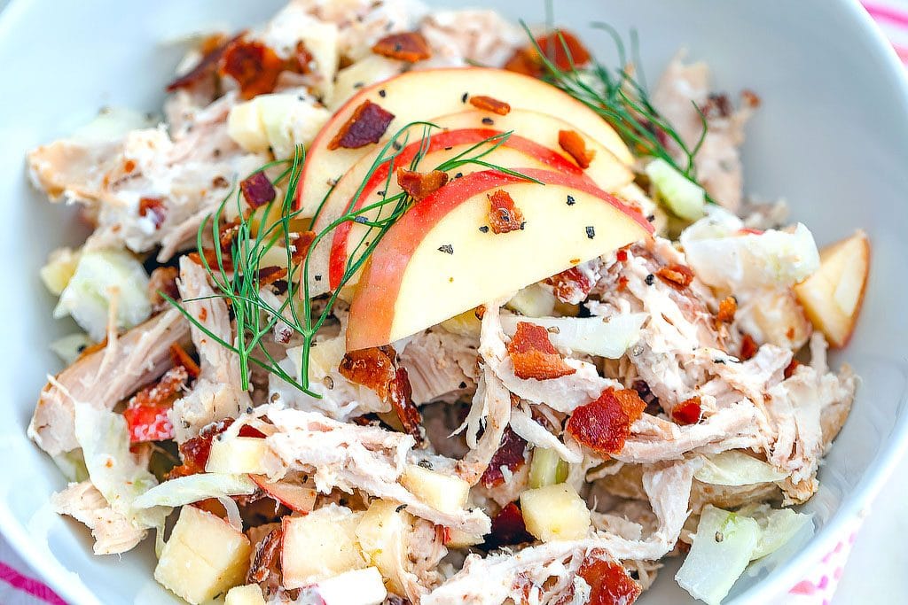 Closeup landscape view of apple, fennel, and bacon chicken salad topped with sliced apples and fennel fronds