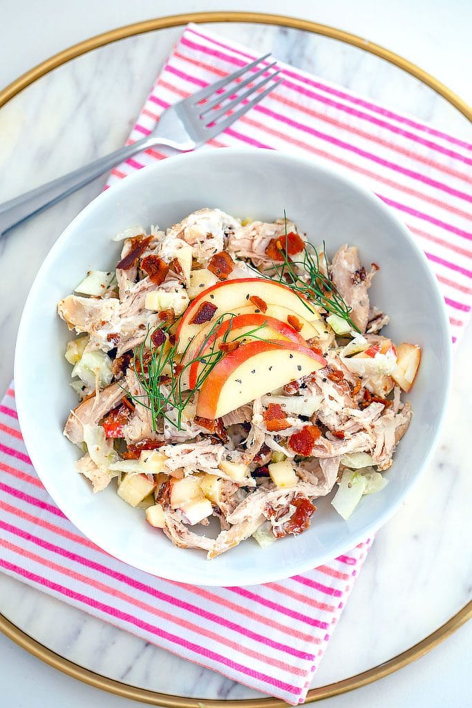 Overhead view of apple, fennel, and bacon chicken salad on a pink and red towel on a marble surface with a fork