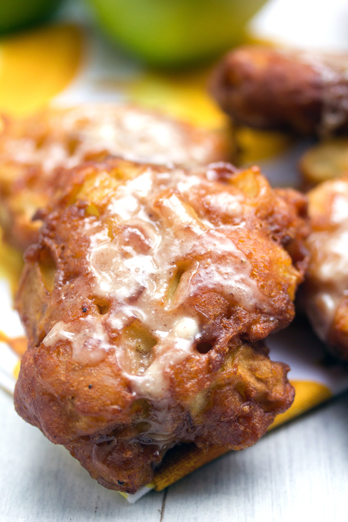 Overhead closeup view of an apple fritter drizzled with icing with more fritters in the background