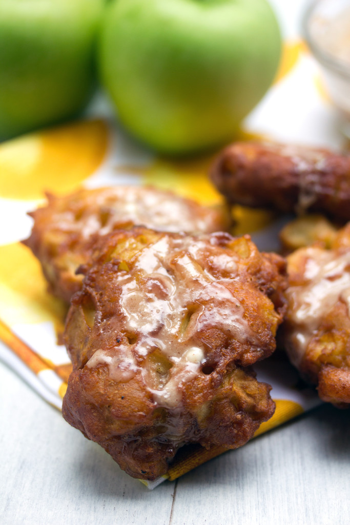 Head-on view of an apple fritter with icing with more fritters and granny smith apples in the background