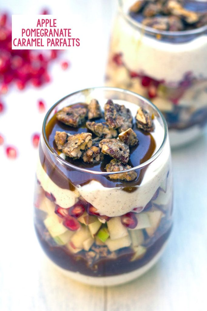 Overhead view of an apple pomegranate caramel yogurt parfait topped with cinnamon sugar pecans with second parfait and pomegranate arils in background with recipe title at top