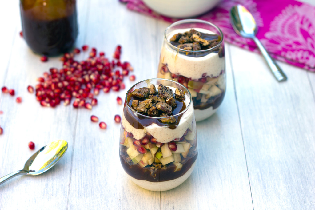 Landscape overhead view of two apple pomegranate caramel yogurt parfait with spoons, pomegranate arils, and jar of caramel in background