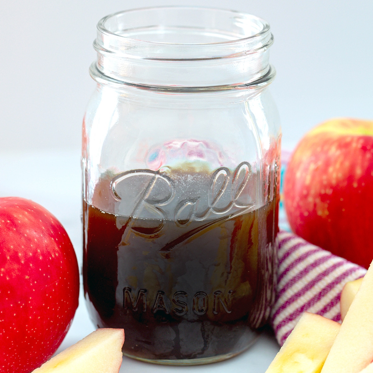 Close-up view of a mason jar of apple simple syrup with apples all around