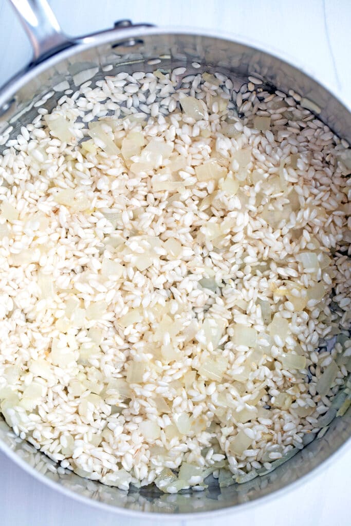 Overhead view of arborio rice in saucepan with onion