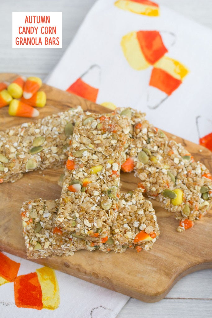 Overhead view of candy corn granola bars on a wooden board with candy corn in background on a candy corn tea towel with recipe title at top