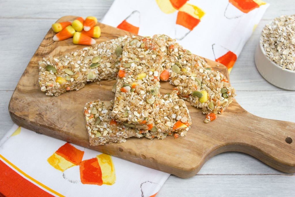 Wooden board with candy corn granola bars on it with candy corn in background.