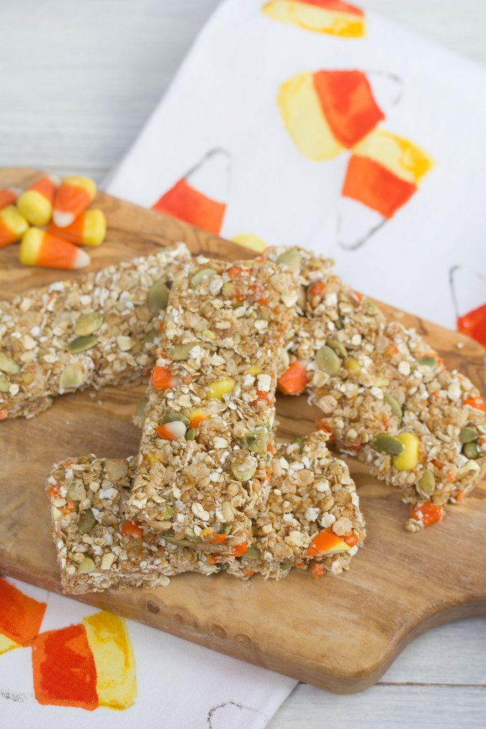 Overhead view of candy corn granola bars on a wooden board with candy corn in background on a candy corn tea towel