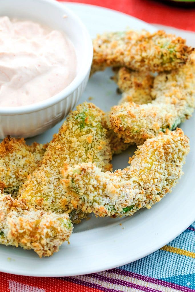 Close up of panko-coated avocado fries with a white bowl full of sriracha dipping sauce