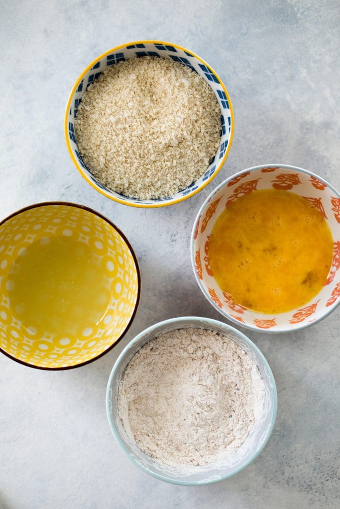 Four bowls filled with avocado fries dredging ingredients- lime juice, flour, egg wash, and panko