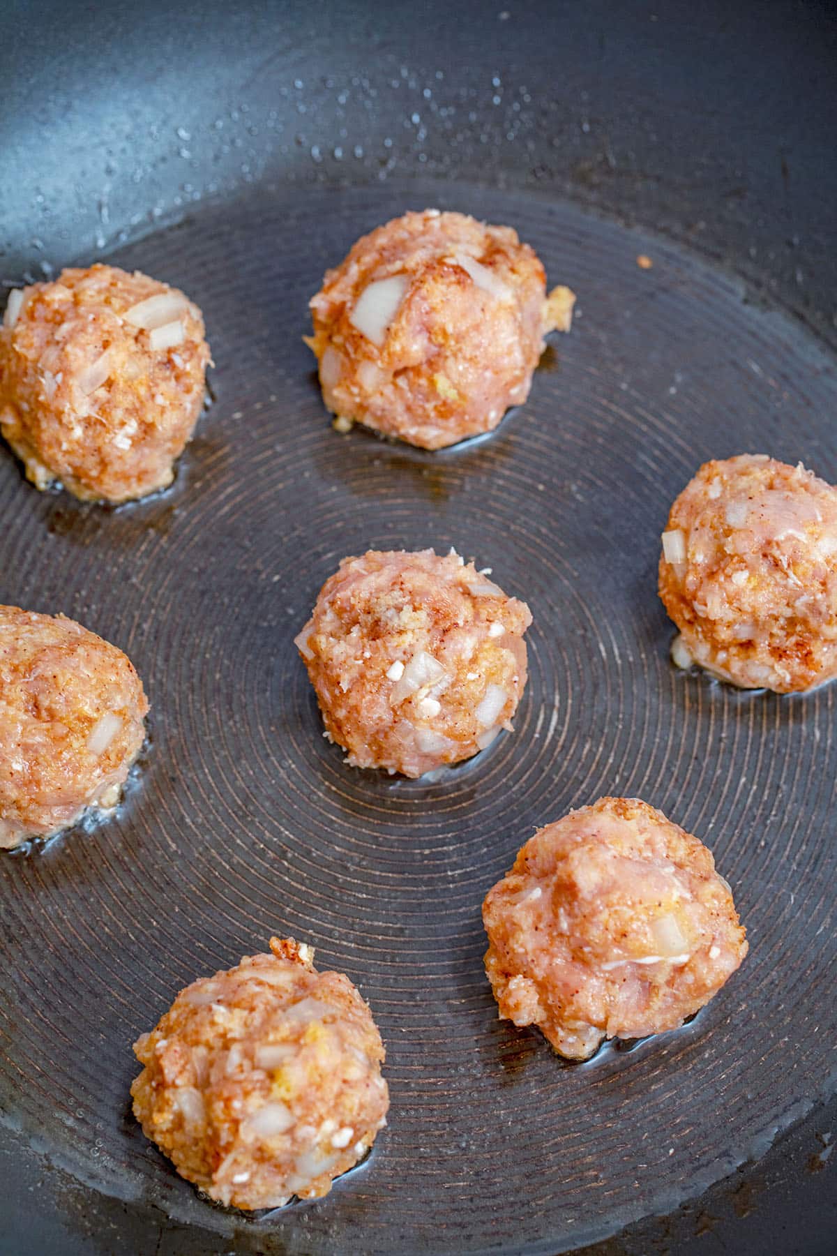 Meatballs formed into golf ball sized balls and cooking in olive oil in skillet.