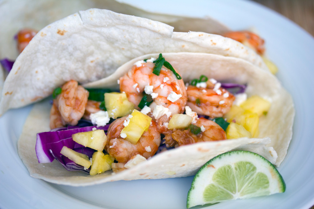 Landscape closeup view of a BBQ shrimp taco on a white plate with a lime wedge