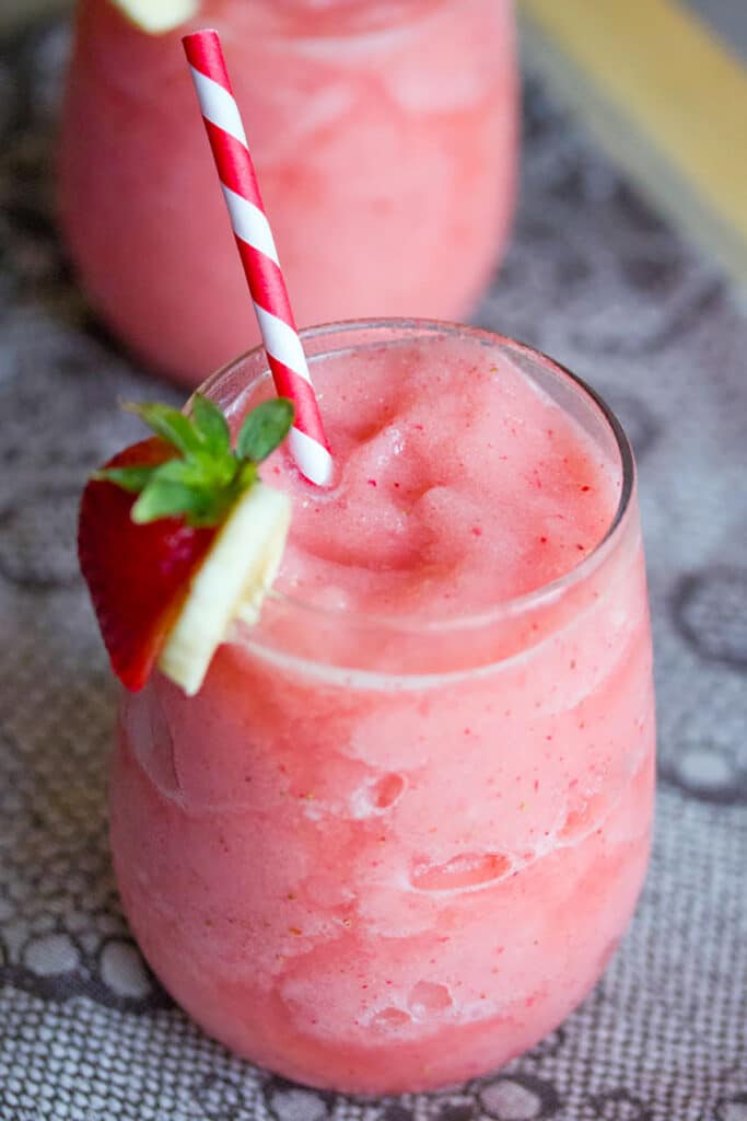 From above view of frozen Strawberry Banana Daiquiri with red and white striped straw and strawberry and banana garnish