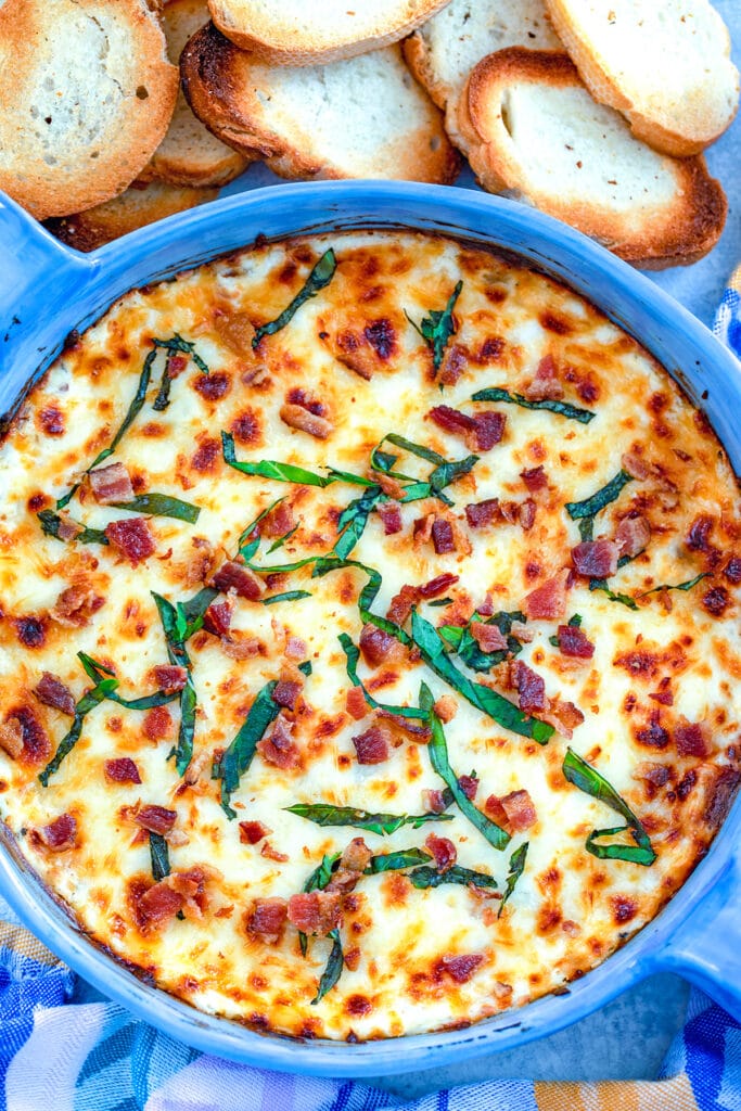 Bird's eye view of bacon white pizza dish topped with basil in a blue pie dish surrounded by crostini