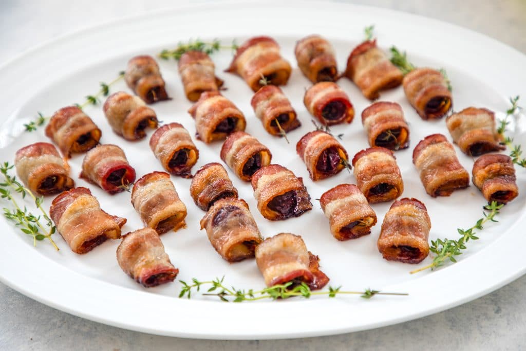 Landscape view of platter with lots of bacon wrapped cherries with thyme and thyme sprig garnishes around the edges