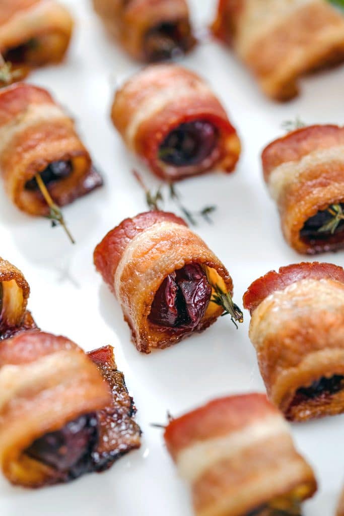 Close-up of platter of bacon wrapped cherries with thyme on white plate