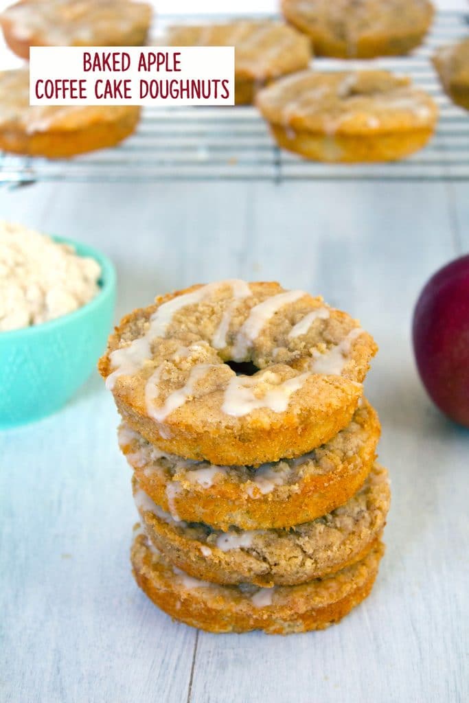 Head-on view of a stack of four baked apple coffee cake doughnuts with a metal rack with more doughnuts in the background and recipe title at top