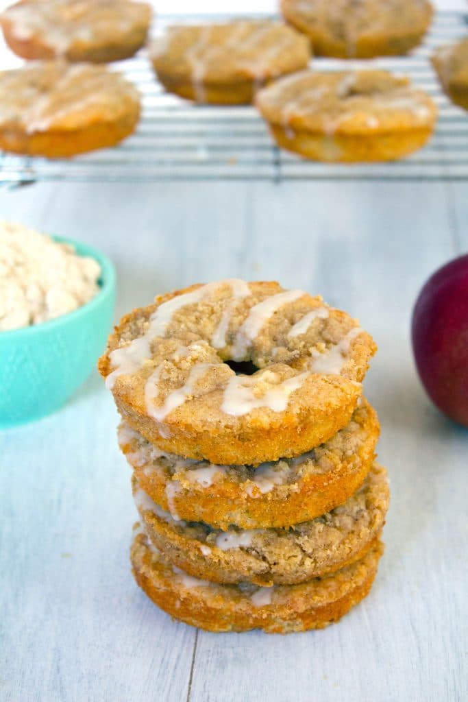 Head-on view of a stack of four baked apple coffee cake doughnuts with a metal rack with more doughnuts in the background