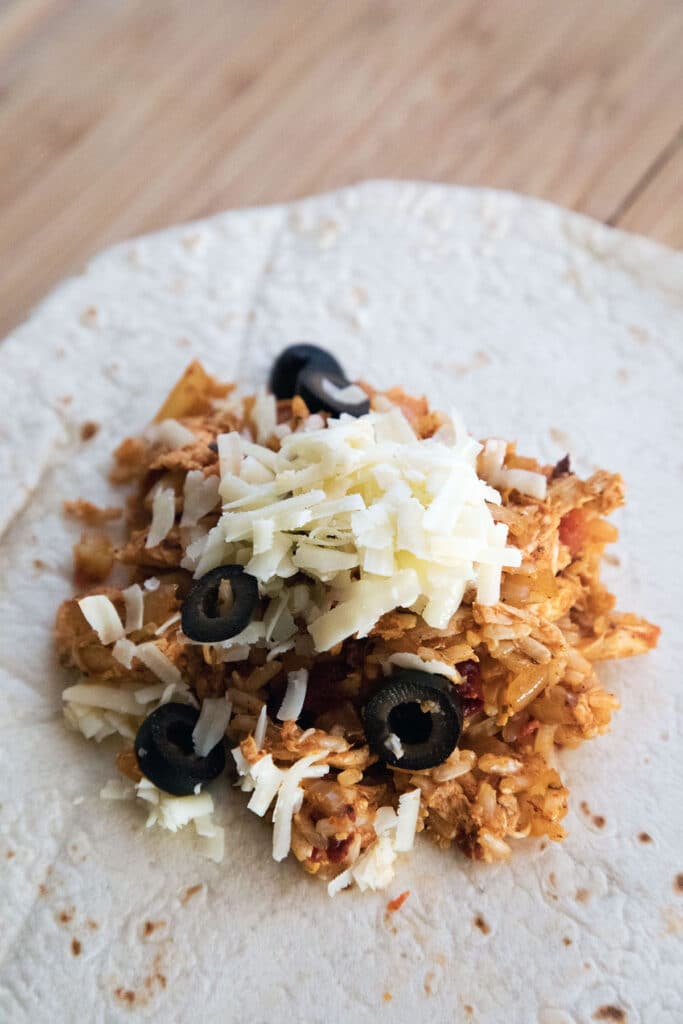 Overhead view of chicken and rice filling, cheese, and olives in the middle of a flour tortilla