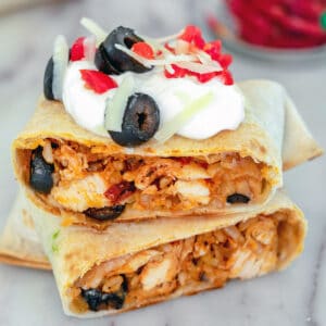 Head-on view of a baked chicken chimichanga cut in half and topped with sour cream, tomatoes, cheese, and olives