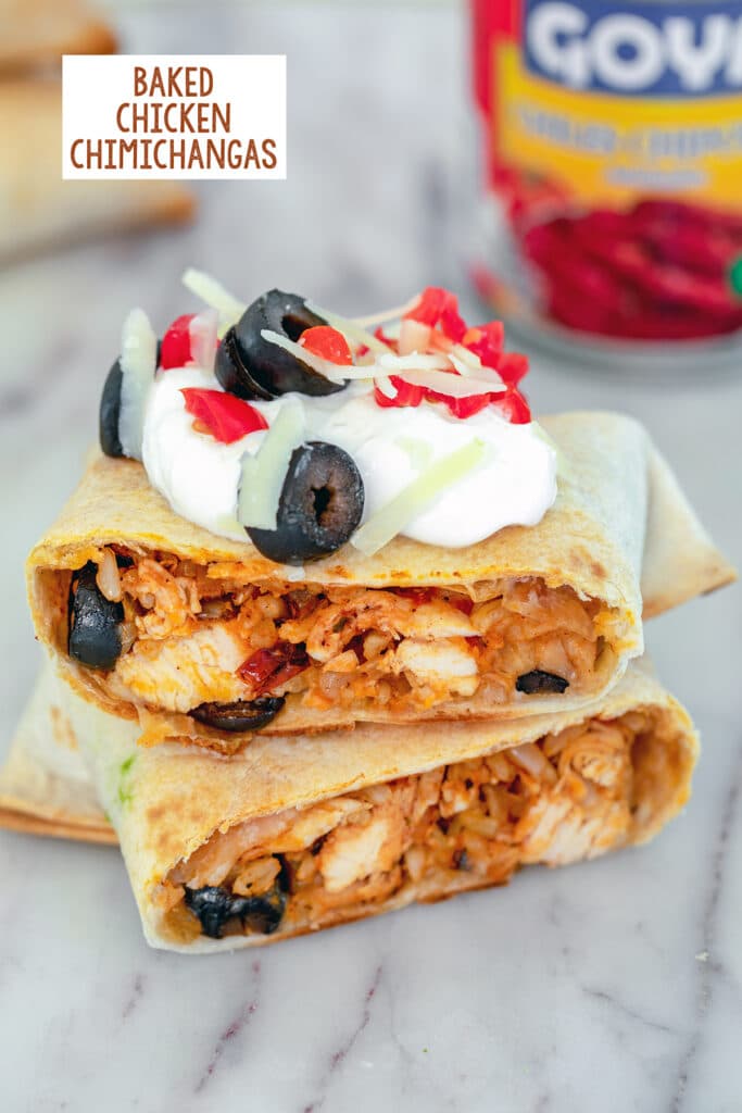 Head-on view of a baked chicken chimichanga cut in half and topped with sour cream, tomatoes, cheese, and olives, with can of chipotle peppers in background and recipe title at top