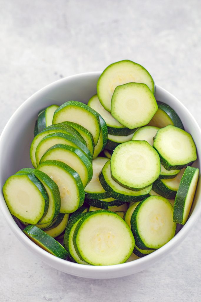 Overhead view of a white bowl filled with thinly sliced zucchini