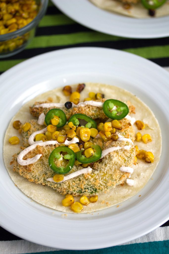 Overhead view of baked avocado tacos with jalapeño, grilled corn, and Greek yogurt sauce on a white plate