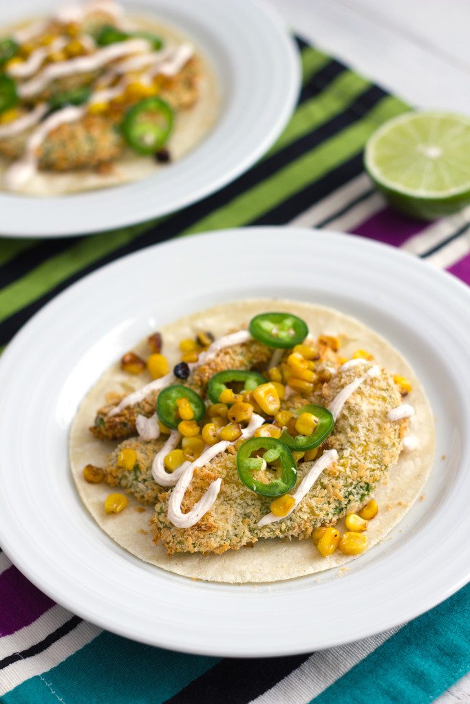 Overhead view of avocado baked taco with jalapeños, grilled corn, and Greek yogurt sauce on a large white plate with second taco and sliced lime in the background