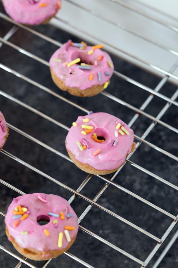 Mini donuts with pink frosting and sprinkles on baking rack