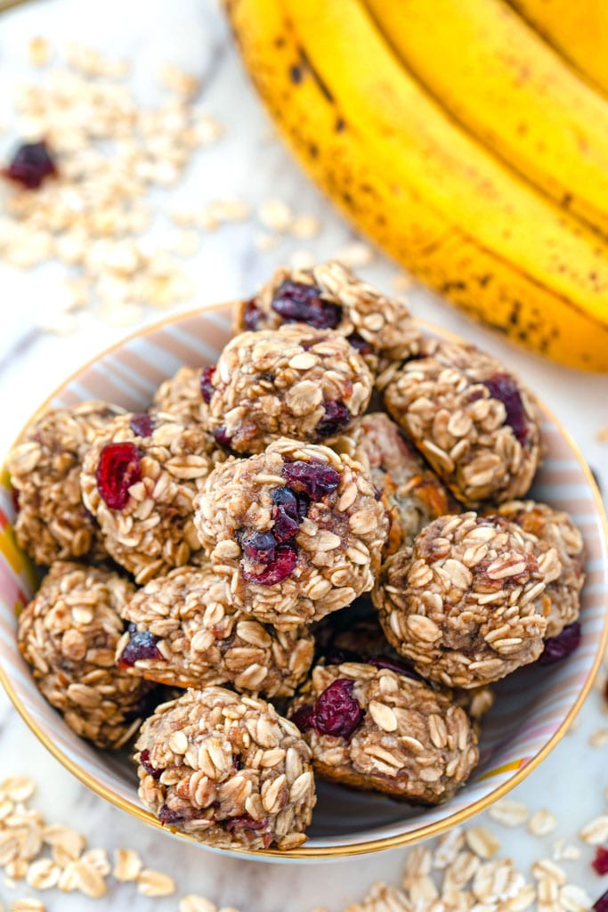 Overhead view of banana maple cranberry cookies in a bowl surrounded by oats and dried cranberries with bananas in background