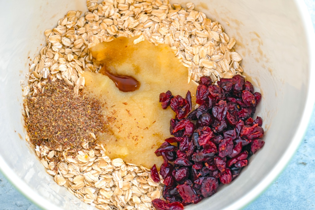 Overhead view of all the healthy cookie ingredients in a bowl, including oats, flaxseed meal, applesauce, maple syrup, and dried cranberries