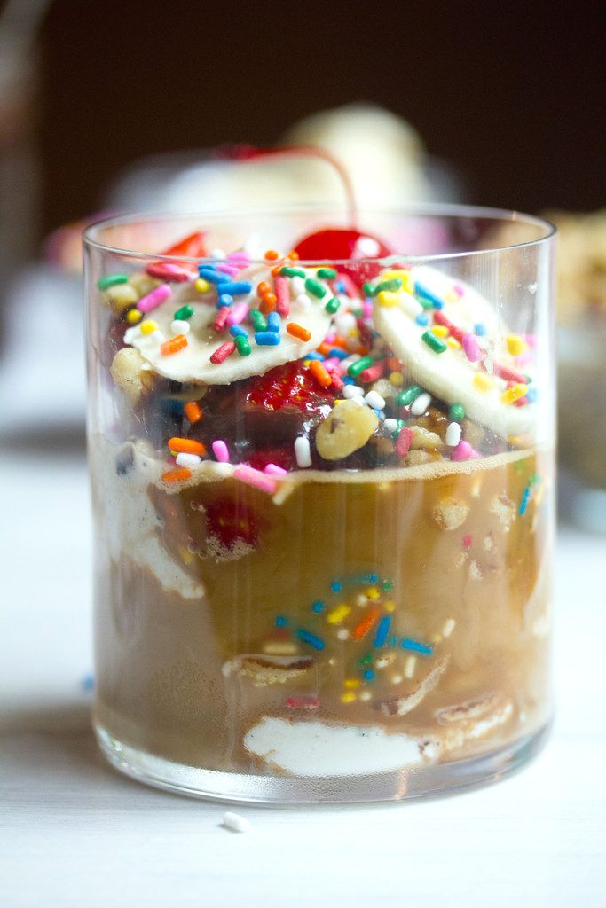 Close up shot of banana split affogato with sliced bananas, strawberries, nuts, sprinkles, and a cherry on top