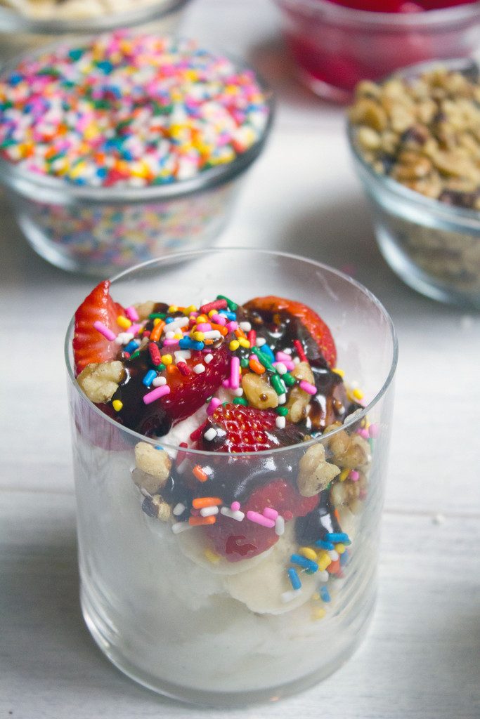 From the top view of banana split affogato with lots of sprinkles, strawberries, nuts, and chocolate sauce and sprinkles and nuts in the background