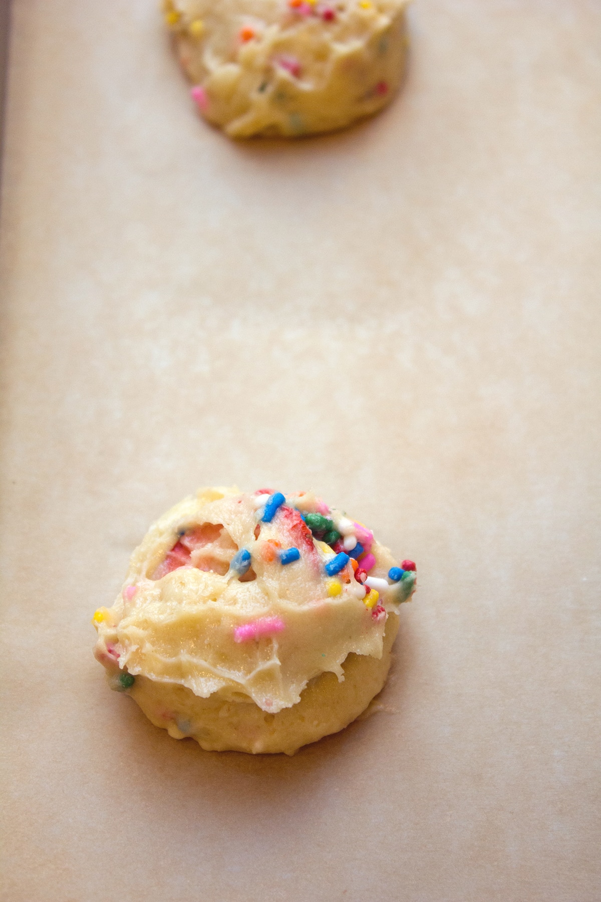 Cookie dough balls with rainbow sprinkles on parchment paper-lined baking sheet.