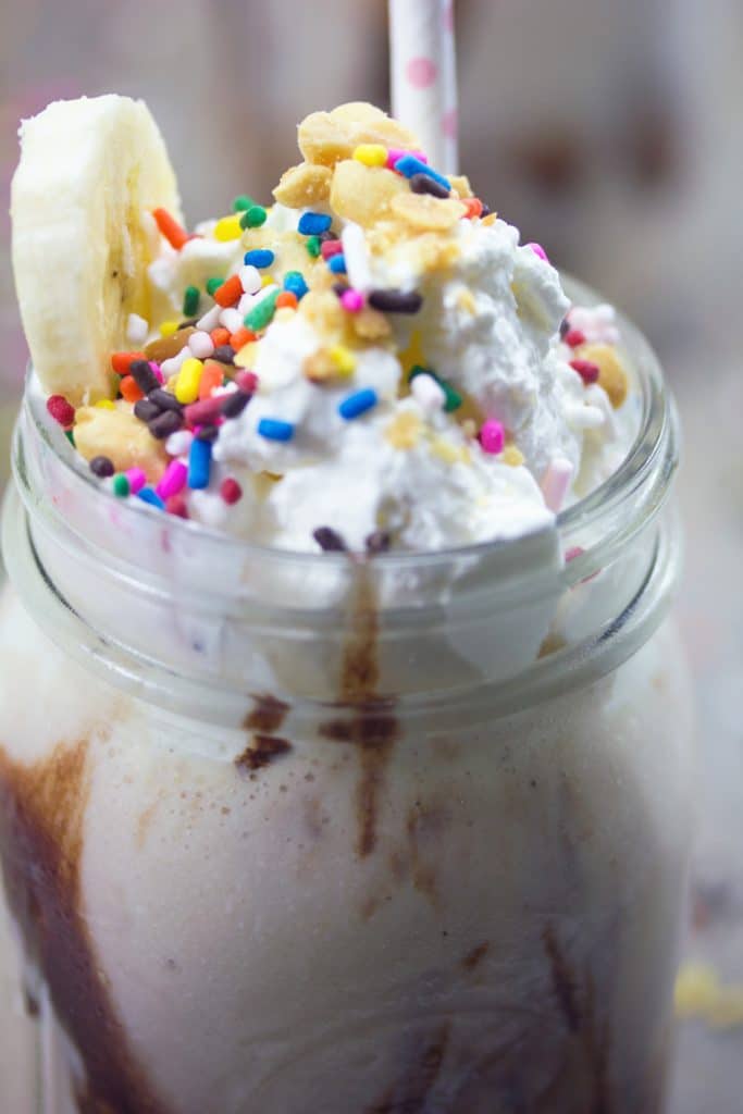 Closeup view of banana split vodka milkshake in a mason jar with whipped cream, sprinkles, peanuts, and banana slicce