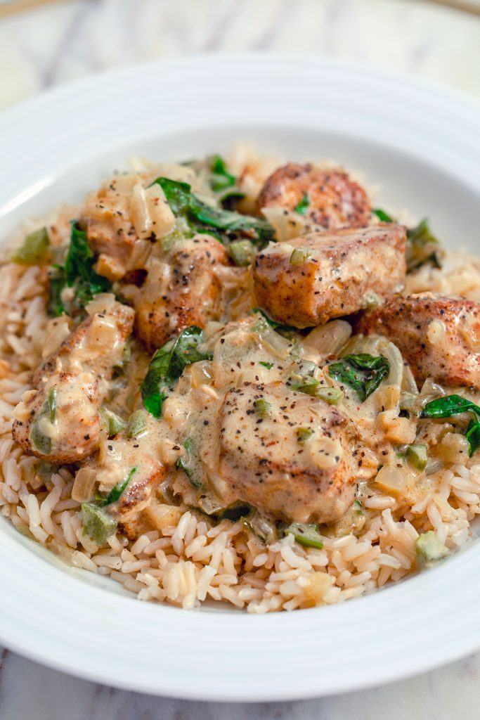 Head on view of basil chicken in coconut curry sauce sitting on a bed of brown rice in a white bowl