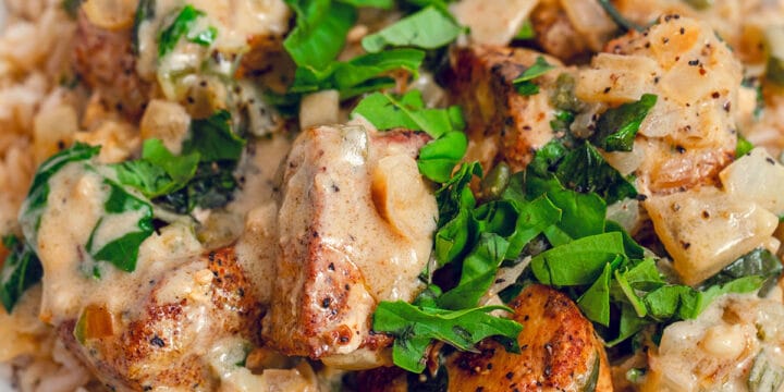 Close-up view of basil chicken in coconut curry sauce with fresh basil in white bowl