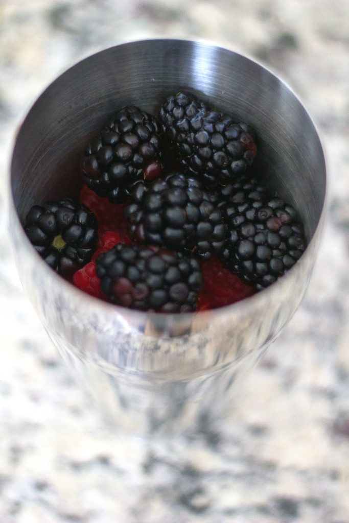 An arial view of a cocktail shaker filled with raspberries and blackberries