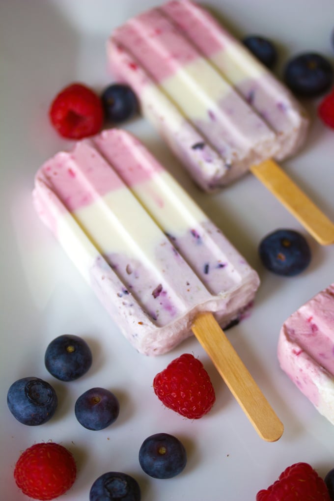 Overhead view of Berry Greek Yogurt Popsicles on a white plate surrounded by blueberries and raspberries