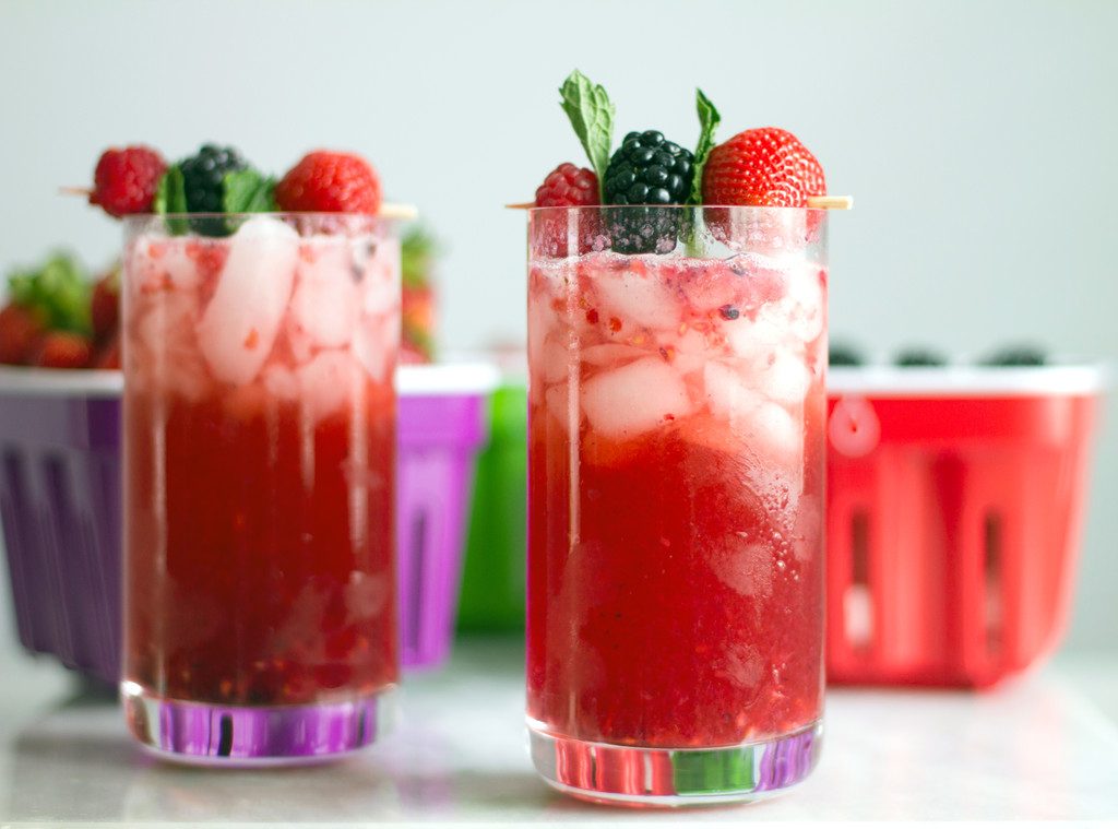 A head on view of two red berry cocktails with lots of ice and berry and mint garnishes