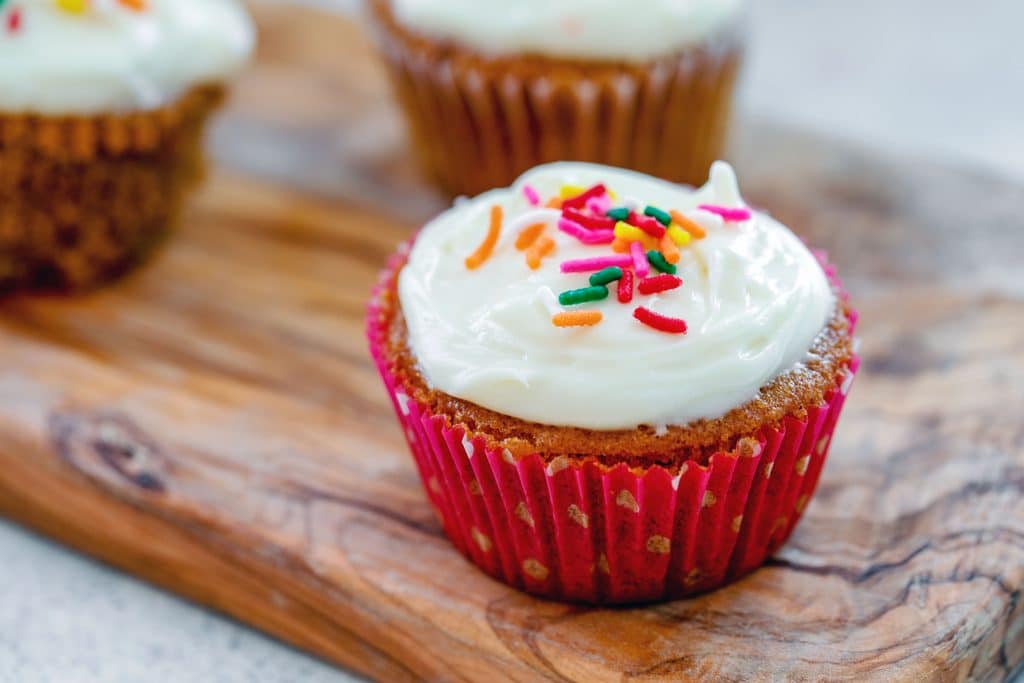 Landscape view of Bethenny Frankel's not-so-red velvet cupcakes with rainbow sprinkles on wooden board