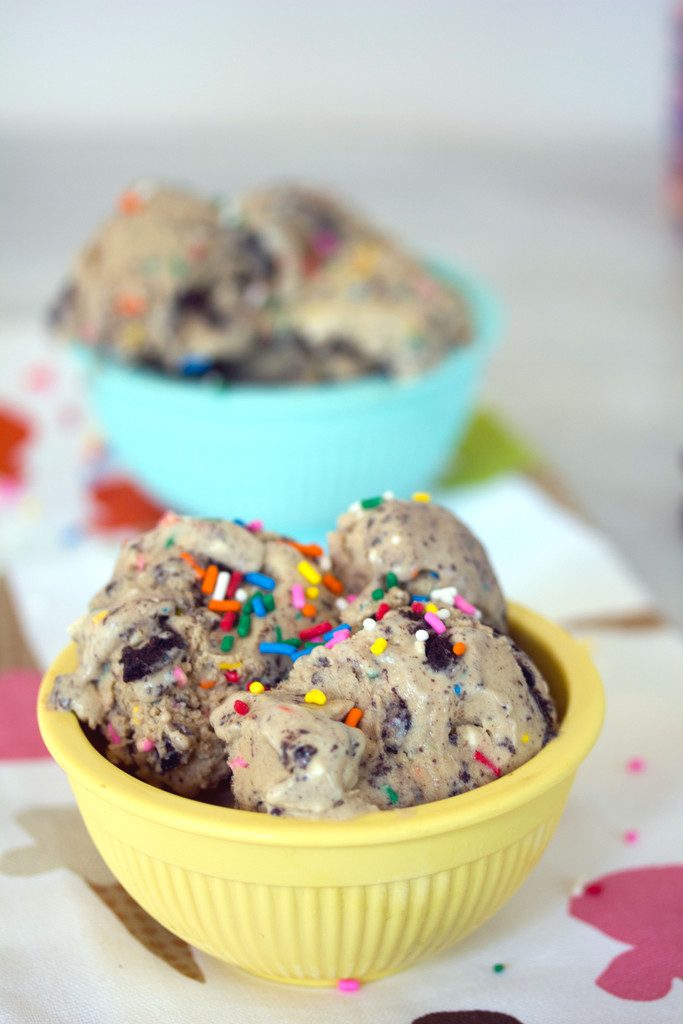 Head-on closeup view of coffee birthday cake Oreo ice cream topped with rainbow sprinkles with second blue bowl of ice cream in the background