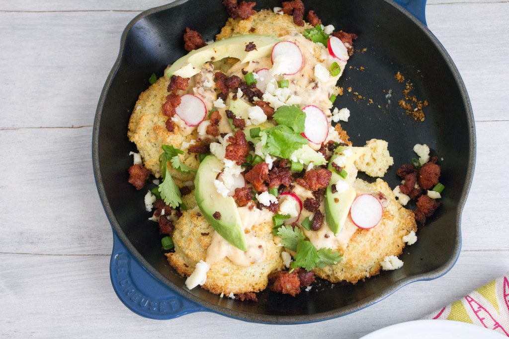 Landscape bird's eye view of skillet with cornmeal biscuits and chorizo gravy topped with avocado, radishes, cheese, cilantro, and scallions