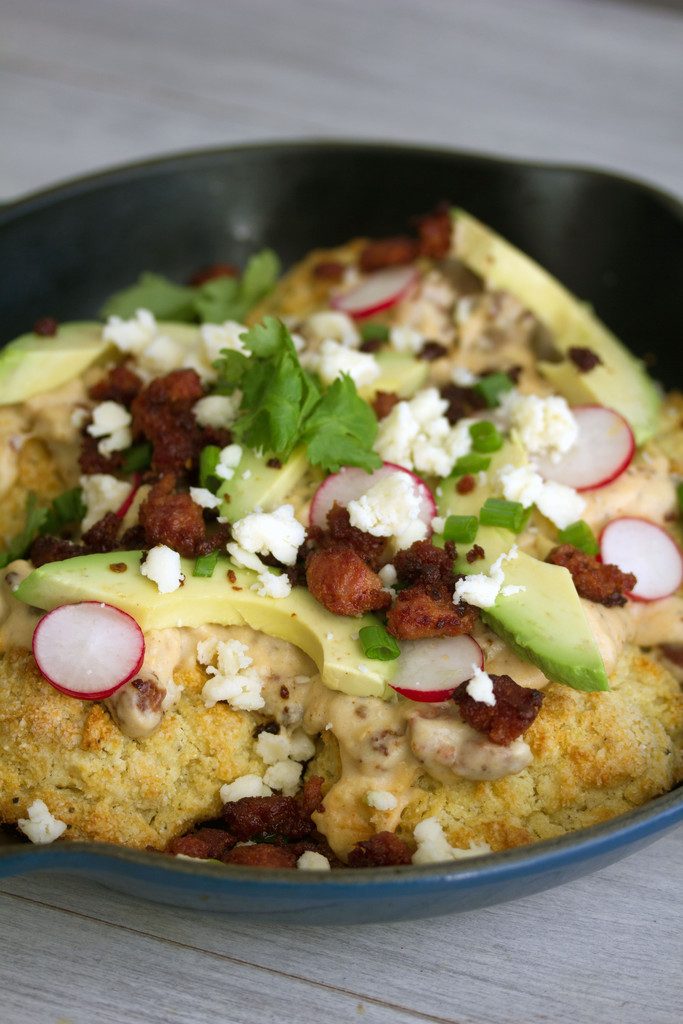 Overhead view of skillet with cornmeal biscuits and chorizo and gravy topped with radishes, avocado, cheese, cilantro, and scallions