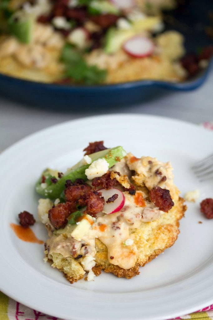 Close-up view of a cornmeal biscuit with chorizo gravy topped with radishes, cheese, and avocado