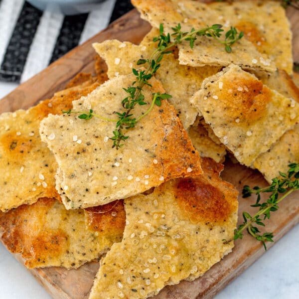 Overhead closeup of black pepper and thyme olive oil crackers on a wooden cutting board with sprigs of thyme